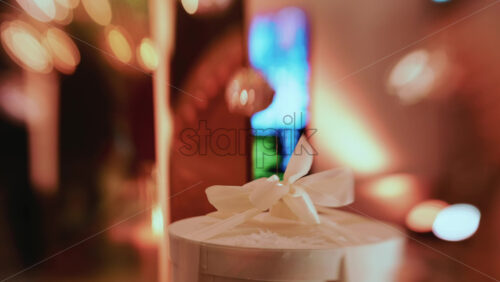 Video - Golden Christmas baubles hanging from a structure alongside a suspended white gift box, with people blurred in the background