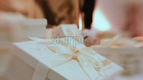 Video - Golden Christmas baubles hanging from a structure alongside a suspended white gift box, with people blurred in the background