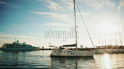 Video - Cannes, France - December 22, 2025: A white sailboat anchored in a marina with larger yachts in the background, under clear daylight and calm waters
