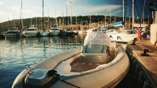 Video - An inflatable motorboat tied to a dock in a busy marina, with sailboats and yachts reflected in calm water under soft afternoon light
