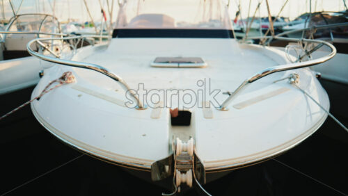 Video - Front view of a white motorboat bow secured to the dock, showing metal railings, ropes, and nautical details in soft daylight