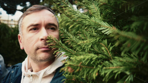 Video - Close up portrait of an adult man standing outdoors surrounded by dense green foliage, partially framed by leaves