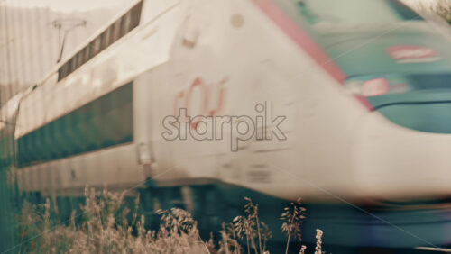 Video - Side view of a passenger train moving along railway tracks through an urban environment, with industrial textures and city elements visible in the background