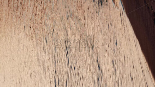 Video - Gentle sea waves rolling onto a sandy beach during sunset, with anchored sailboats visible on the horizon. Vertical