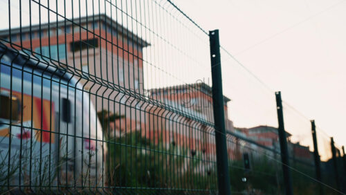 Video - Passenger train passing through, framed by overhead electric cables and surrounding buildings