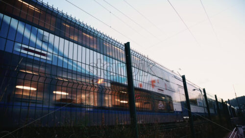 Video - Passenger train passing through, framed by overhead electric cables and surrounding buildings