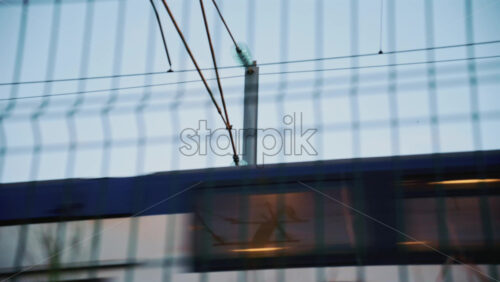 Video - Passenger train passing through, framed by overhead electric cables and surrounding buildings