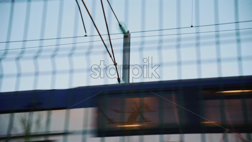 Video - Passenger train passing through, framed by overhead electric cables and surrounding buildings