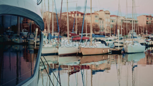 Video - Sailboats and yachts docked in a calm marina, reflected in still water with pastel colored residential buildings in the background