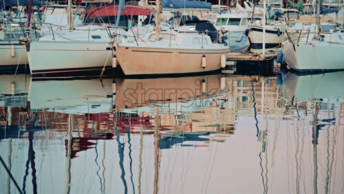 Video - Sailboats and yachts docked in a calm marina, reflected in still water with pastel colored residential buildings in the background