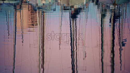 Video - Close up of rippling water reflecting sailboat masts and harbor structures, forming abstract vertical patterns