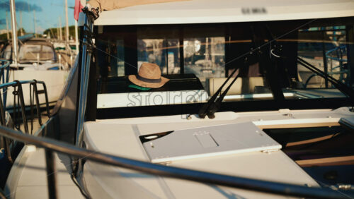 Video - Close up of a straw hat placed inside the cockpit of a moored motorboat, with marina details softly blurred in the background