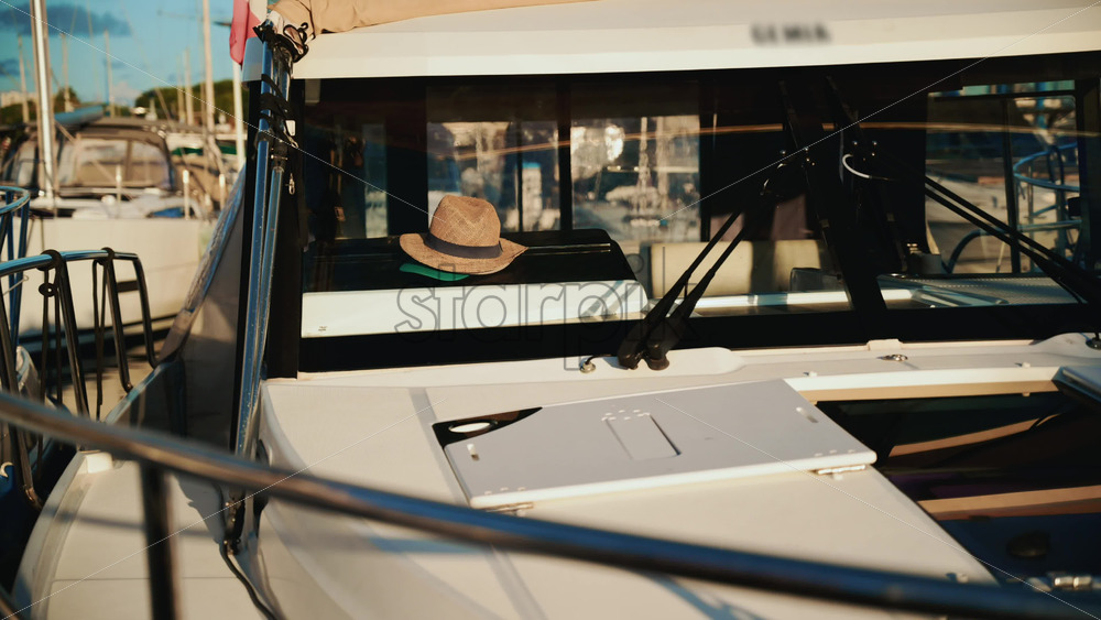 Video - Close up of a straw hat placed inside the cockpit of a moored motorboat, with marina details softly blurred in the background