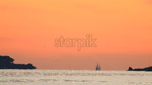 Video - Wide seascape showing a distant vessel on the horizon beneath an orange sunset sky, with calm water
