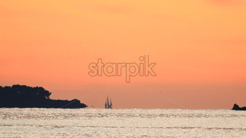 Video - Wide seascape showing a distant vessel on the horizon beneath an orange sunset sky, with calm water