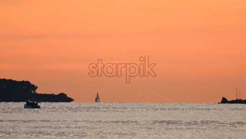Video - Wide seascape showing a distant vessel on the horizon beneath an orange sunset sky, with calm water