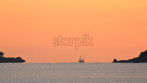 Video - Wide seascape showing a distant vessel on the horizon beneath an orange sunset sky, with calm water