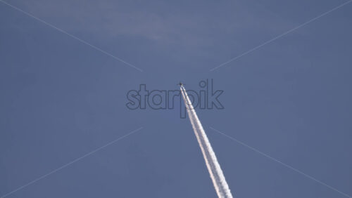 Video - Passenger airplane flying high in a clear blue sky, leaving a long white vapor trail behind