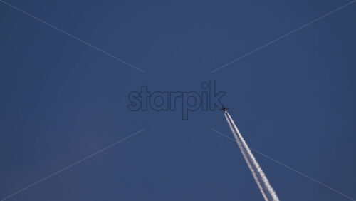 Video - Passenger airplane flying high in a clear blue sky, leaving a long white vapor trail behind
