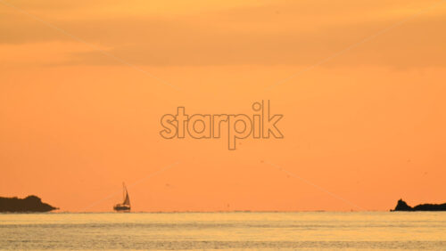Video - Wide seascape showing a distant vessel on the horizon beneath an orange sunset sky, with calm water