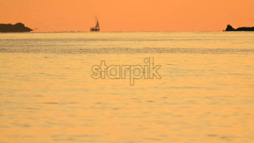 Video - Wide seascape showing a distant vessel on the horizon beneath an orange sunset sky, with calm water