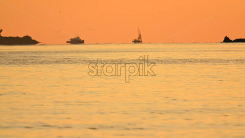 Video - Wide seascape showing a distant vessel on the horizon beneath an orange sunset sky, with calm water