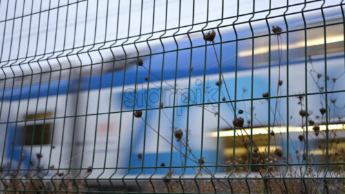 Video - Passenger train passing through, framed by overhead electric cables and surrounding buildings