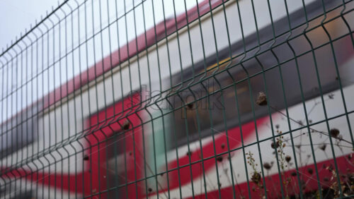 Video - Passenger train passing through, framed by overhead electric cables and surrounding buildings
