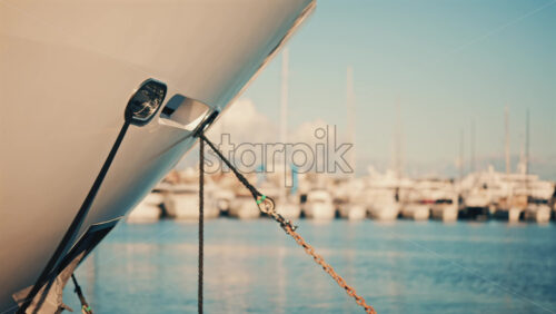 Video - Close up of a yacht bow tied with a rope at a marina, with boats softly blurred in the background
