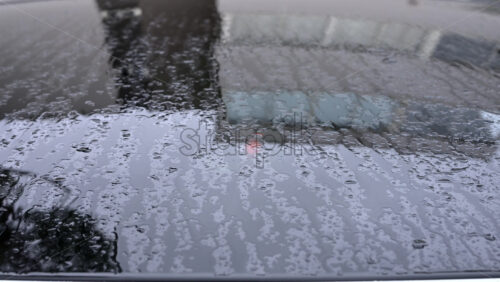 Video - Close up of raindrops covering a car roof during rainfall, with blurred reflections of surrounding buildings