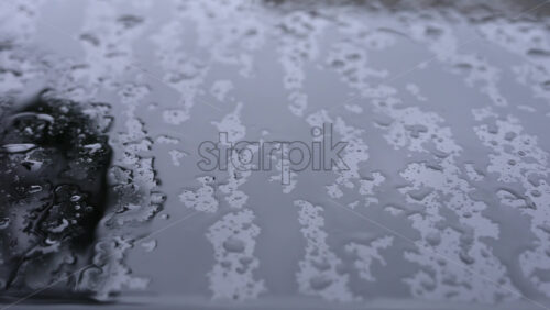 Video - Close up of raindrops covering a car roof during rainfall, with blurred reflections of surrounding buildings
