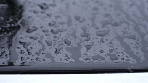 Video - Close up of raindrops covering a car roof during rainfall, with blurred reflections of surrounding buildings