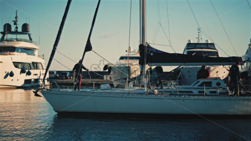 Video - Cannes, France - December 12, 2025: Sailboat moving through a marina with several people standing on deck during daylight