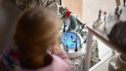 Video - Young child with mom pointing at a detailed Christmas village miniature with ice skaters and snow covered trees