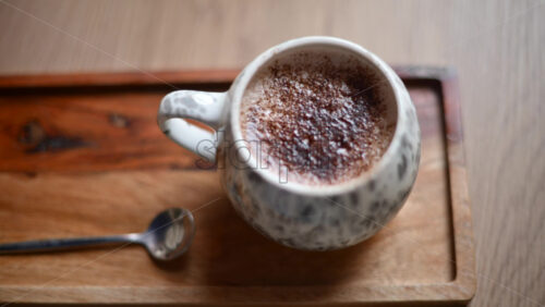 Video - Close up of a ceramic cup filled with hot chocolate topped with cocoa powder, placed on a wooden tray