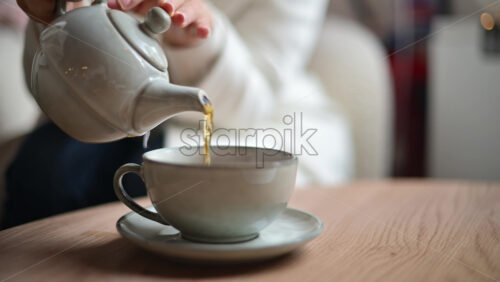 Video - Close up of tea being poured from a ceramic teapot into a matching cup on a wooden table