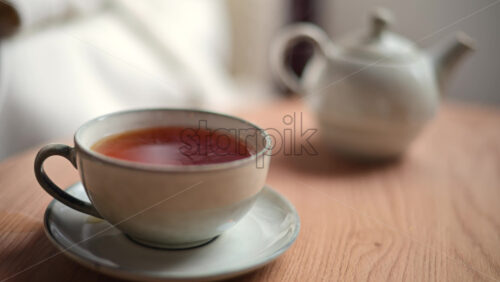 Video - Close up of a ceramic cup filled with hot tea placed on a matching saucer on a wooden table