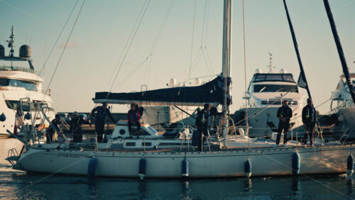 Video - Cannes, France - December 12, 2025: Sailboat moving through a marina with several people standing on deck during daylight