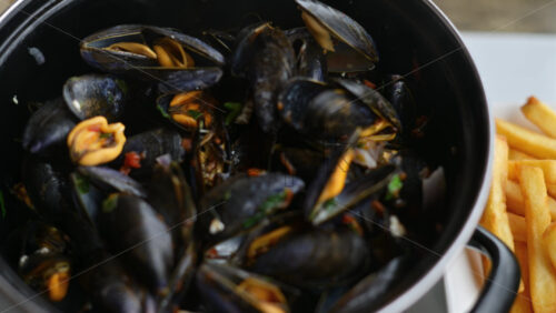 Video - Cooked mussels served in a pot with herbs and sauce, accompanied by golden fries on the side