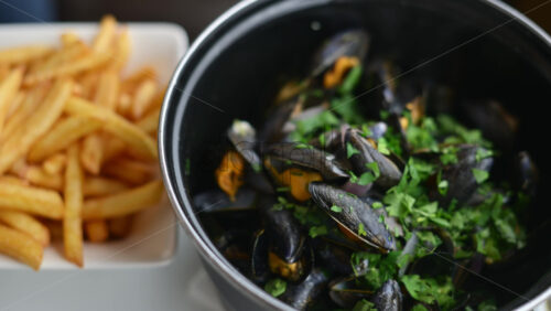 Video - Cooked mussels served in a pot with herbs and sauce, accompanied by golden fries on the side