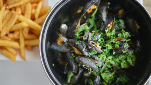 Video - Cooked mussels served in a pot with herbs and sauce, accompanied by golden fries on the side