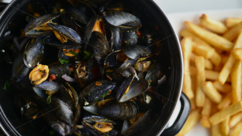 Video - Cooked mussels served in a pot with herbs and sauce, accompanied by golden fries on the side
