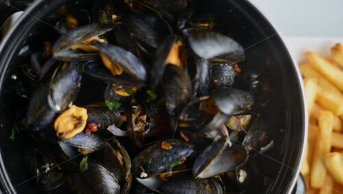 Video - Cooked mussels served in a pot with herbs and sauce, accompanied by golden fries on the side