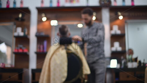 Video - Blurred view of a barber cutting a client's hair inside a modern barbershop
