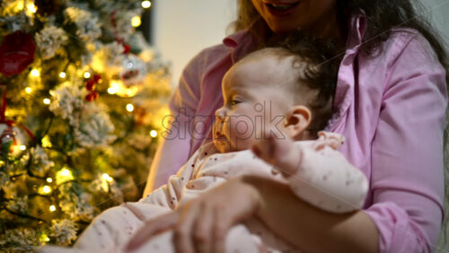 Video - Mother holding a baby indoors next to a decorated and illuminated Christmas tree