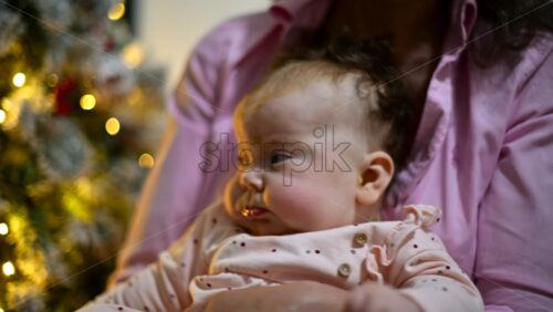 Video - Mother holding a baby indoors next to a decorated and illuminated Christmas tree