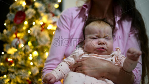 Video - Mother holding a baby indoors next to a decorated and illuminated Christmas tree