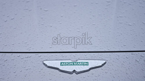 Video - Cannes, France - December 23, 2025: Close up view of an Aston Martin logo on a luxury sports car with rain droplets on the surface
