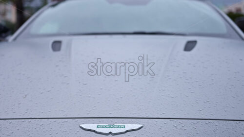 Video - Cannes, France - December 23, 2025: Close up view of an Aston Martin logo on a luxury sports car with rain droplets on the surface