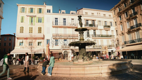 Video - Cannes, France - December 23, 2025: People sitting and relaxing around a water fountain in a lively square